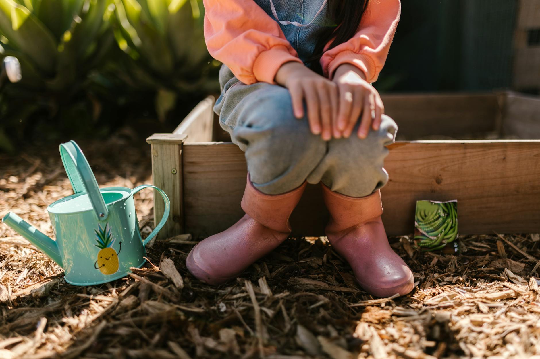 a child sitting in rubber boots sitting on a wooden plant box